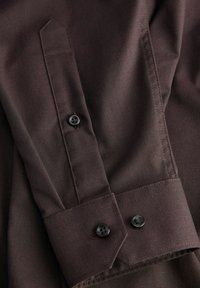 Donkerbruine stoffen overhemddetail met een op maat gemaakte manchet met twee zwarte knopen, gestructureerd weefsel en een puntige manchetstijl.