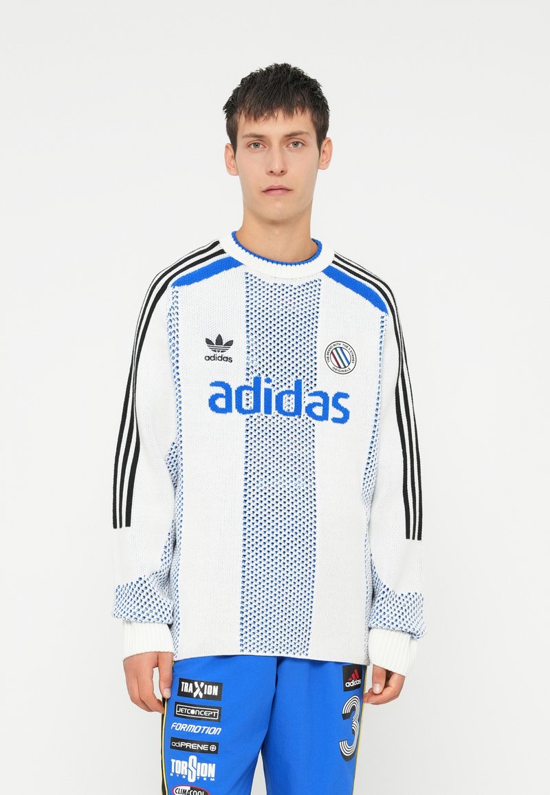 Pleteni pulover z modrimi detajli, belim telesom in teksturiranim vzorcem. Opremljen z logotipom Adidas in tremi črnimi črtami vzdolž rokavov.