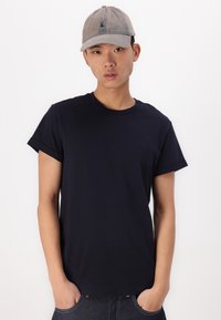 Navy blue cotton t-shirt with short sleeves and a round neckline. Worn with a gray cap featuring a logo at the front. Plain design.
