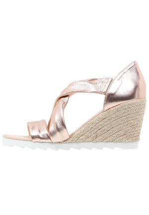 Sandał na koturnie z metalicznym, różowo-złotym syntetycznym wierzchem, plecioną platformą z juty i białą gumową podeszwą; posiada skrzyżowane paski zapewniające pewne dopasowanie.