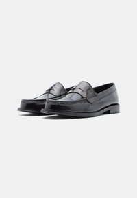 Mocassins en cuir noir avec une finition brillante, des détails cousus sur le dessus, un petit talon et une forme classique et épurée.
