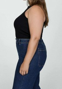 Haut noir sans manches associé à un jean en denim bleu taille haute. Le jean présente un style classique à cinq poches et une coupe droite.