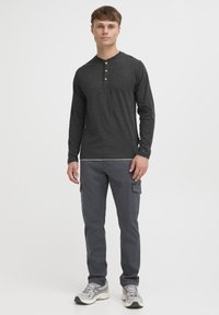 Langarm, donkergrijze henley-shirt met drie houten knopen bij de hals, gecombineerd met grijze cargo-broek en lichtgrijze sneakers.