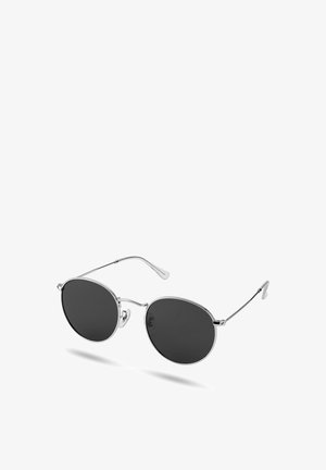 Runde solbriller med svarte linser, tynne sølvfargede metallrammer og justerbare nesepolstringer, vist mot en hvit bakgrunn.