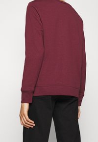 Sudadera burdeos con un corte relajado, puños acanalados y cuello redondo. Presenta una textura suave y un detalle de costura mínimo.