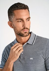 Grå polo skjorta med en texturerad tyg, med en kontrasterande marinblå krage och vita randiga accenter, samt en liten logotyp på bröstet.