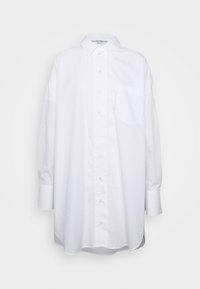 Camisa blanca de manga larga, con cuello puntiagudo, un bolsillo en el pecho y puños abotonados, sobre un fondo sencillo.