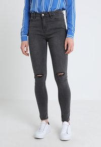 Jeans ajustados de tiro alto en gris con detalles desgastados en las rodillas, combinados con una camisa de rayas azul y blanca y zapatillas blancas.