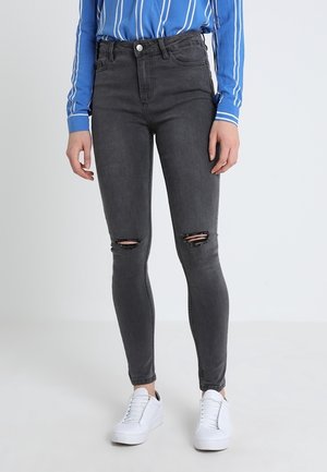 Jeans ajustados de tiro alto en gris con detalles desgastados en las rodillas, combinados con una camisa de rayas azul y blanca y zapatillas blancas.