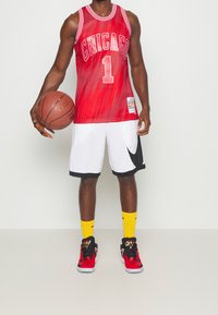 Punainen koripallopaita, jossa lukee "CHICAGO" ja numero "1", valkoiset shortsit mustilla yksityiskohdilla, keltaiset sukat ja punaiset lenkkarit. Koripallo on pidetty yhdessä kädessä.