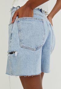 Shorts en denim bleu clair avec ourlet effiloché, déchirures sur le devant et poches arrière. La texture du tissu est un denim classique avec une légère élasticité.