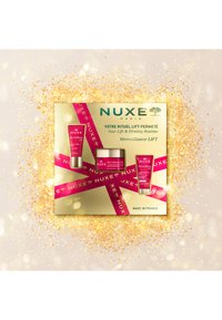 Zestaw kosmetyków NUXE w złotym pudełku o błyszczącym wykończeniu, zawierający trzy różowe tubki i słoiczki, przyozdobiony gorącą różową wstążką.