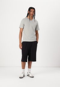Grå stribet kortærmet T-shirt, sorte knælange shorts, hvide sneakers med sorte detaljer og grå sokker. Minimalistisk afslappet outfit.