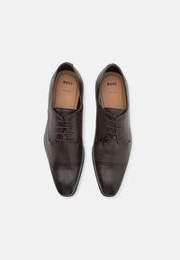 Chaussures habillées en cuir marron à lacets avec une finition lisse et texturée, embout pointu et détails de couture subtils. Logo "BOSS" visible à l'intérieur.