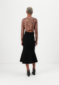 Leopard print cropped top with long sleeves, paired with a black, fitted, flared midi skirt. Worn with high-heeled black shoes.