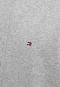 Sudadera gris hecha de un tejido suave que presenta un pequeño logo bordado en colores azul marino, blanco y rojo en el pecho.