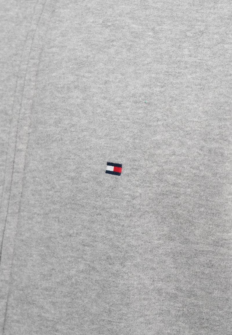 Sudadera gris hecha de un tejido suave que presenta un pequeño logo bordado en colores azul marino, blanco y rojo en el pecho.
