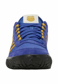 Chaussure de sport en suède bleu avec des accents jaunes, des lacets texturés et une semelle extérieure en caoutchouc noir avec un motif en relief. Logo K-Swiss sur la languette.