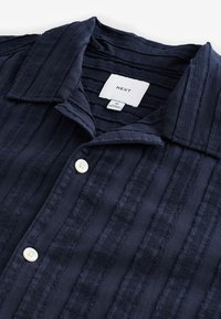 Marineblå kortærmet skjorte med et struktureret stribet mønster, der har en klapkrave og to hvide knapper foran.