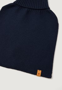 Sötétkék kötött poncsó magas bordázott gallérral, texturált anyaggal és egy kis világosbarna címkével, amelyen csillagmotívum található a peremén.