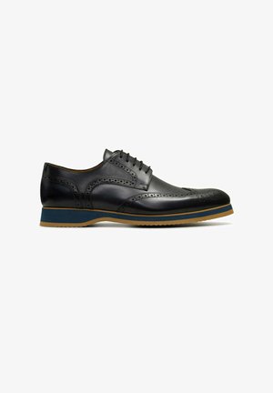 Zwarte lederen wingtip oxford schoen met geperforeerde details en een laag van blauw en bruin in de zool, weergegeven in zijaanzicht op een witte achtergrond.