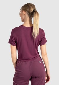 Haut court à manches courtes bordeaux avec un col ras du cou, texture lisse et coupe décontractée. Pantalons bordeaux assortis avec des poches latérales discrètes.