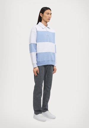 Light blue and gray striped long-sleeve polo with a collar, featuring a zip closure. Paired with dark gray jeans and white sneakers.