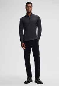 Dark gray long-sleeve pullover with a zip collar, paired with black pants and black lace-up boots, against a plain gray backdrop.
