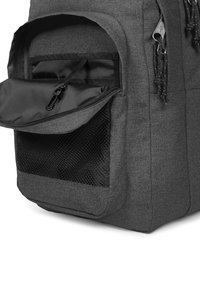 Harmaa kangasreppu, jossa on vetoketjullinen etutasku ja verkkosivutasku. Ulkopinnassa on teksturoitu, kestävä pinta.