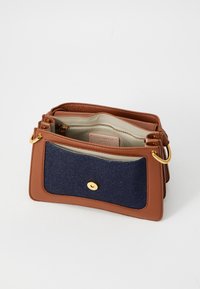 Brun læder håndtaske med en denim frontlomme, en guld knaplukning og to indvendige rum. Udstyret med hardware i guldfarve.