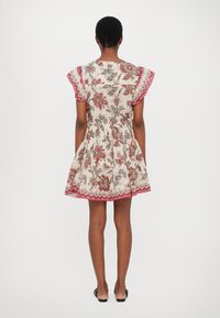 Robe à motif floral avec des manches courtes à volants, une taille cintrée et une jupe évasée. Fond ivoire avec des accents rouges et verts.