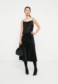 Fekete selymes camisole fekete textúrájú bőrnadrág midi szoknya alá rétegezve. Fekete bokapántos magassarkú cipővel és ráncolt bőr kézitáskával párosítva.
