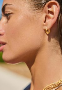 Guld hoop ørering på en slank øre, med en glat tekstur og et rundt design. Huden viser en naturlig glans.