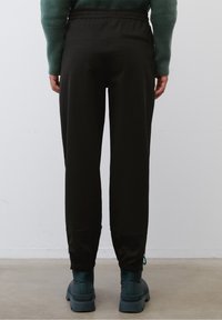 Joggers negros con cintura elástica, piernas ajustadas y puños con cremallera. Fabricados con un tejido suave, cuentan con un bolsillo trasero.