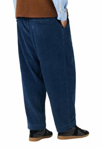 Pantaloni di velluto a coste blu navy con gambe larghe, dotati di tasche laterali e una finitura strutturata, abbinati a scarpe nere.