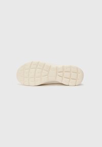 Sole of a sneaker with a textured rubber surface, featuring a grid pattern and rounded edges, in a light cream color.