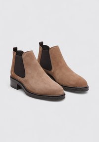 Bottines Chelsea en suede marron avec un talon bas, des panneaux latéraux élastiques et un bout lisse et arrondi. Coutures décoratives le long du bord de la semelle.