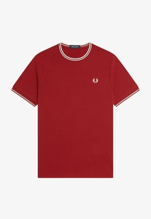 Camiseta roja de manga corta con dobles rayas blancas en el cuello y puños, y pequeño logo de corona de laurel blanca en el pecho izquierdo.