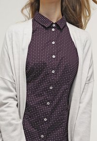 Chemise boutonnée à manches longues, à pois, de couleur violet foncé, avec un col. Associée à un cardigan gris clair. Tissu doux, coupe décontractée.