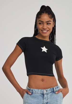T-shirt cropped nera con maniche corte, presentante una grafica di una stella argentata al centro. Cuciture a contrasto stilose lungo i bordi.