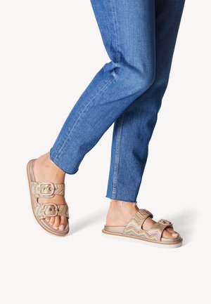 Sandali slide intrecciati in oro e multicolore con due cinturini regolabili e fibbie decorative, abbinati a jeans in denim blu a vita alta e taglio cropped.