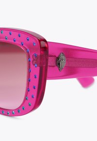 Occhiali da sole in plastica rosa con forma quadrata, caratterizzati da strass blu e verdi lungo la montatura e un accento laterale testurizzato.