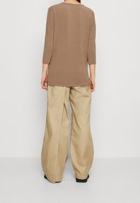 Braunes langärmliges Oberteil mit lockerer Passform, kombiniert mit hellbeigen weiten Hosen. Das Outfit zeichnet sich durch ein einfaches Design und eine weiche Stofftextur aus.