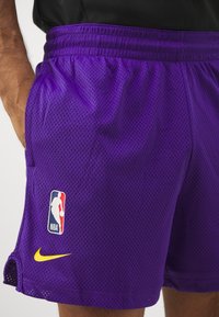 I pantaloni corti da basket in rete viola presentano una vita elasticizzata, tasche laterali a fessura, il logo NBA e un accento giallo del marchio Nike.