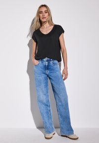 Svart kortärmad blus i kombination med ljusblå vida jeans med hög midja och subtila blekningar, samt beige slip-in skor.