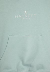 Sudadera de color azul claro con una textura suave, que cuenta con un bolsillo frontal y el logotipo bordado "HACKETT LONDON" en rosa pálido.