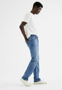 Lichtblauwe denim jeans met een rechte pasvorm, voorzien van een klassieke vijf-pocket ontwerp en een lichte vervaging. Gepaarde met een effen wit t-shirt en witte sneakers.