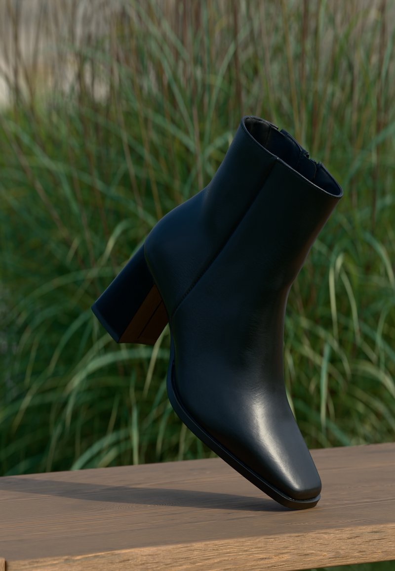 Bottine en cuir noir avec bout pointu, talon bloc et texture lisse. Présente une tige ajustée et un design minimaliste.