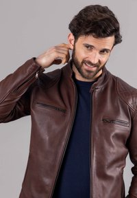 Brown leather jacket with a stand-up collar, zippered pockets, and textured shoulder accents, worn over a navy sweater.