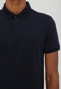 Navy blue polo shirt made of cotton, featuring a classic collar, short sleeves, and a subtle embossed EA7 logo on the chest.